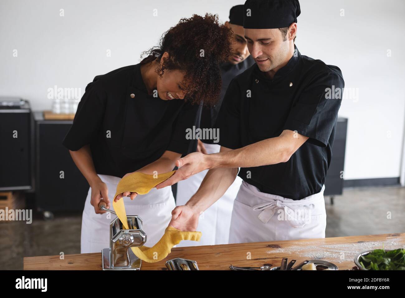 Diverse male and female chef processing pasta sheet in machine at restaurant kitchen Stock Photo