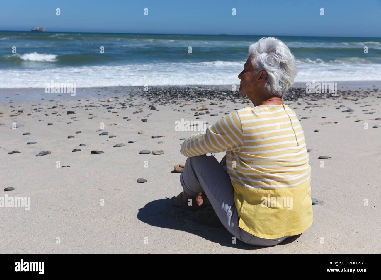 Senior caucasian woman sitting on beach by the sea Stock Photo