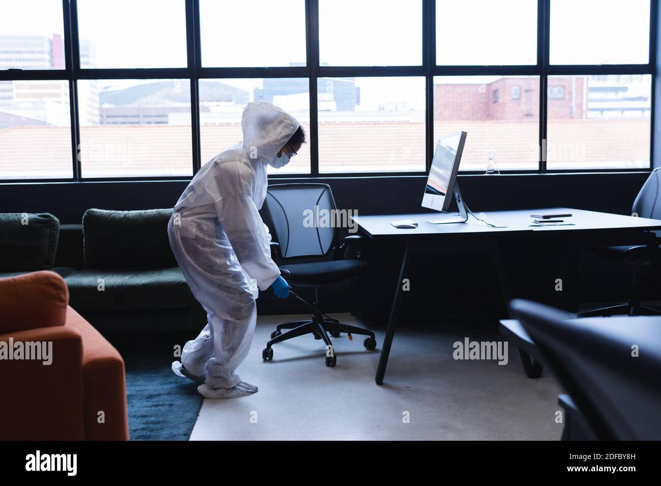 Health worker in protective clothing spraying disinfectant in office Stock Photo