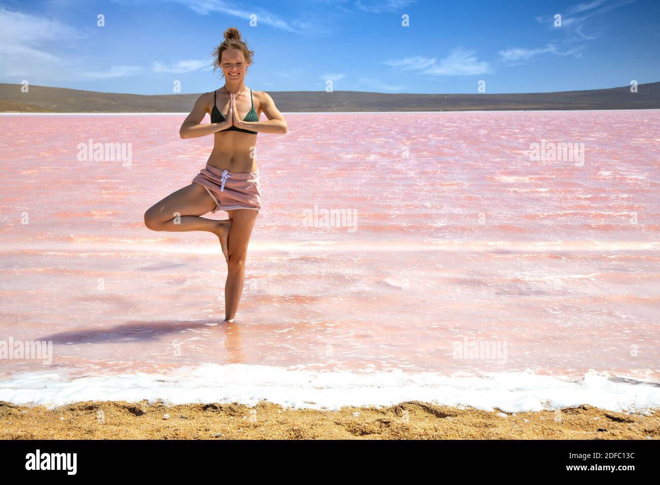 Young elegant woman doing meditation, doing a yoga pose for balance standing on one leg in salty pink lake Stock Photo