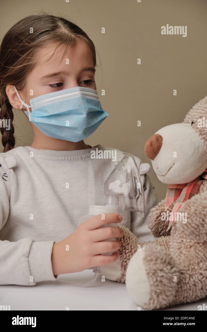 Doctor little girl in mask playing with a toy bear. Child doctor concept. Inhalation Stock Photo