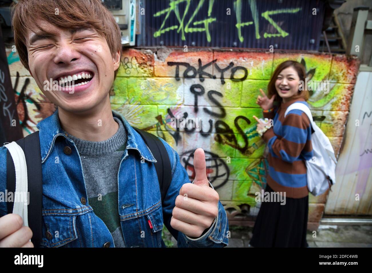 Japan, two young Japanese have fun writing Tokyo is yours on the wall