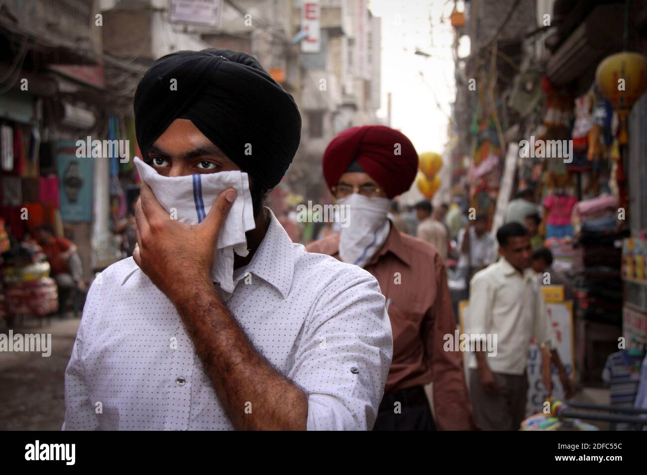 India, Sikh men walk down a street in New Delhi wearing a turban and covering their faces Stock Photo
