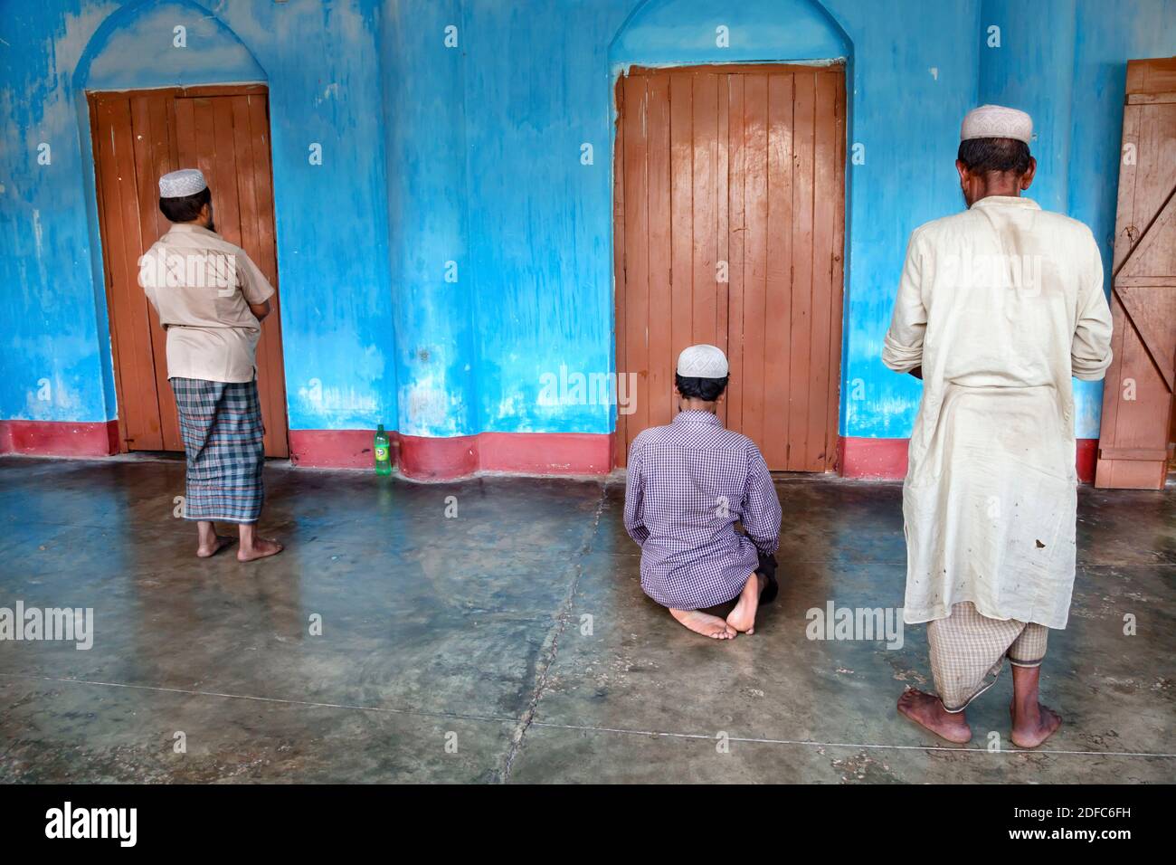 Bangladesh, three muslim men pray at mosque with blue wall in Sreemangal Stock Photo