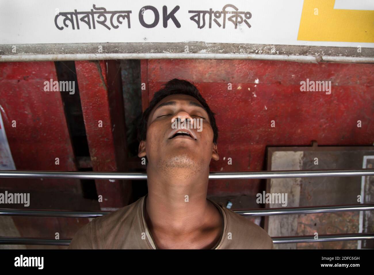 Bangladesh, a tired man sleeps at the bus stop in Chittagong under a sign Stock Photo