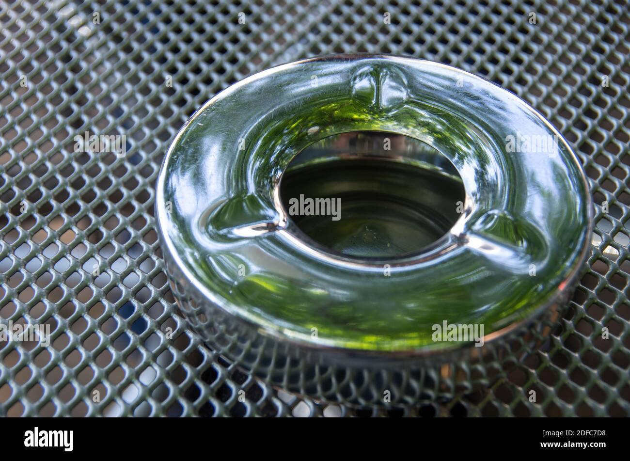 Empty metal ashtray on the surface of a wire mesh table. Stock Photo