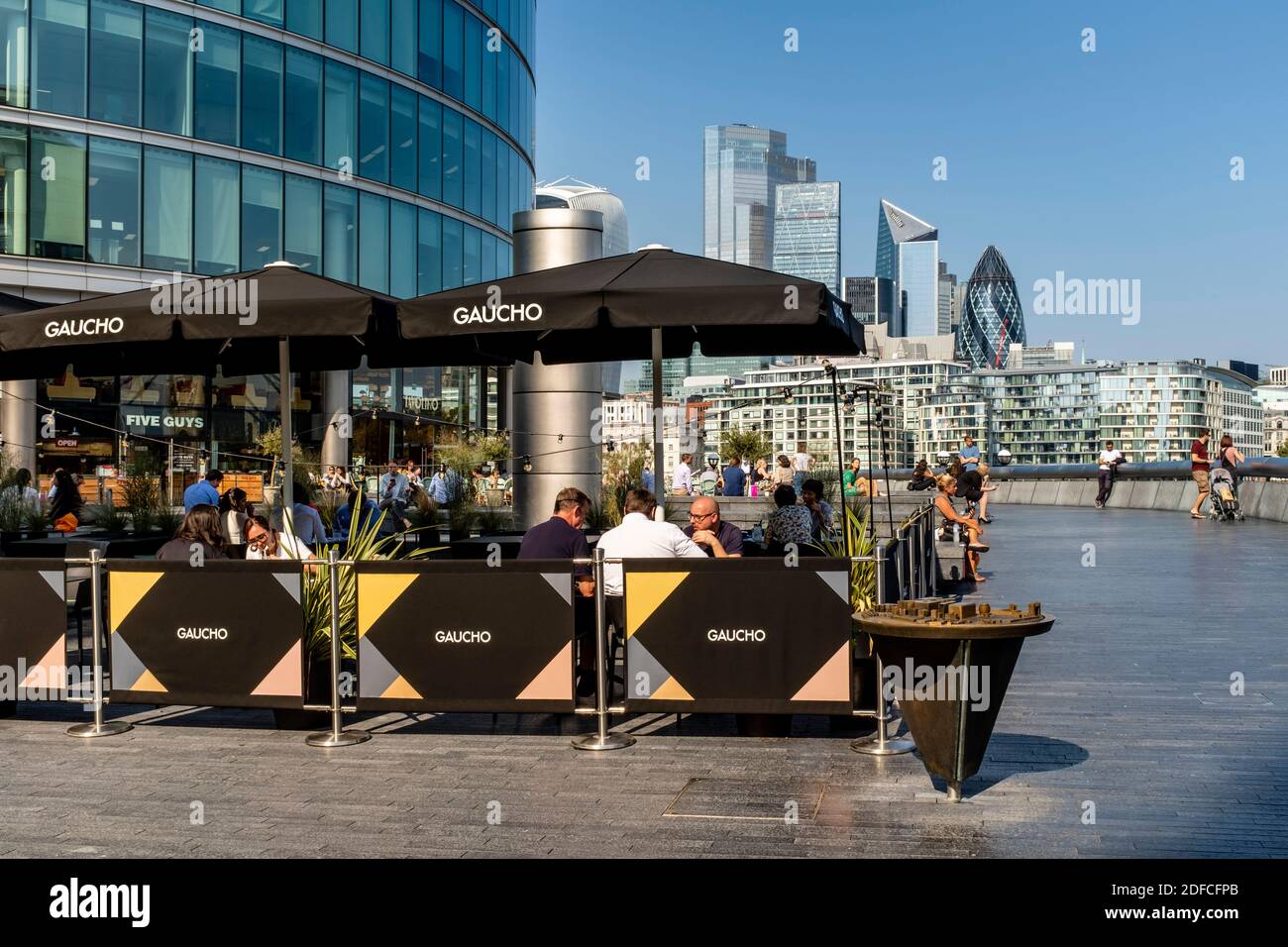 People Eating Outdoors At The Gaucho Restaurant (Tower Bridge) With The City Of London In The Backround, London Bridge City Area, London, UK. Stock Photo