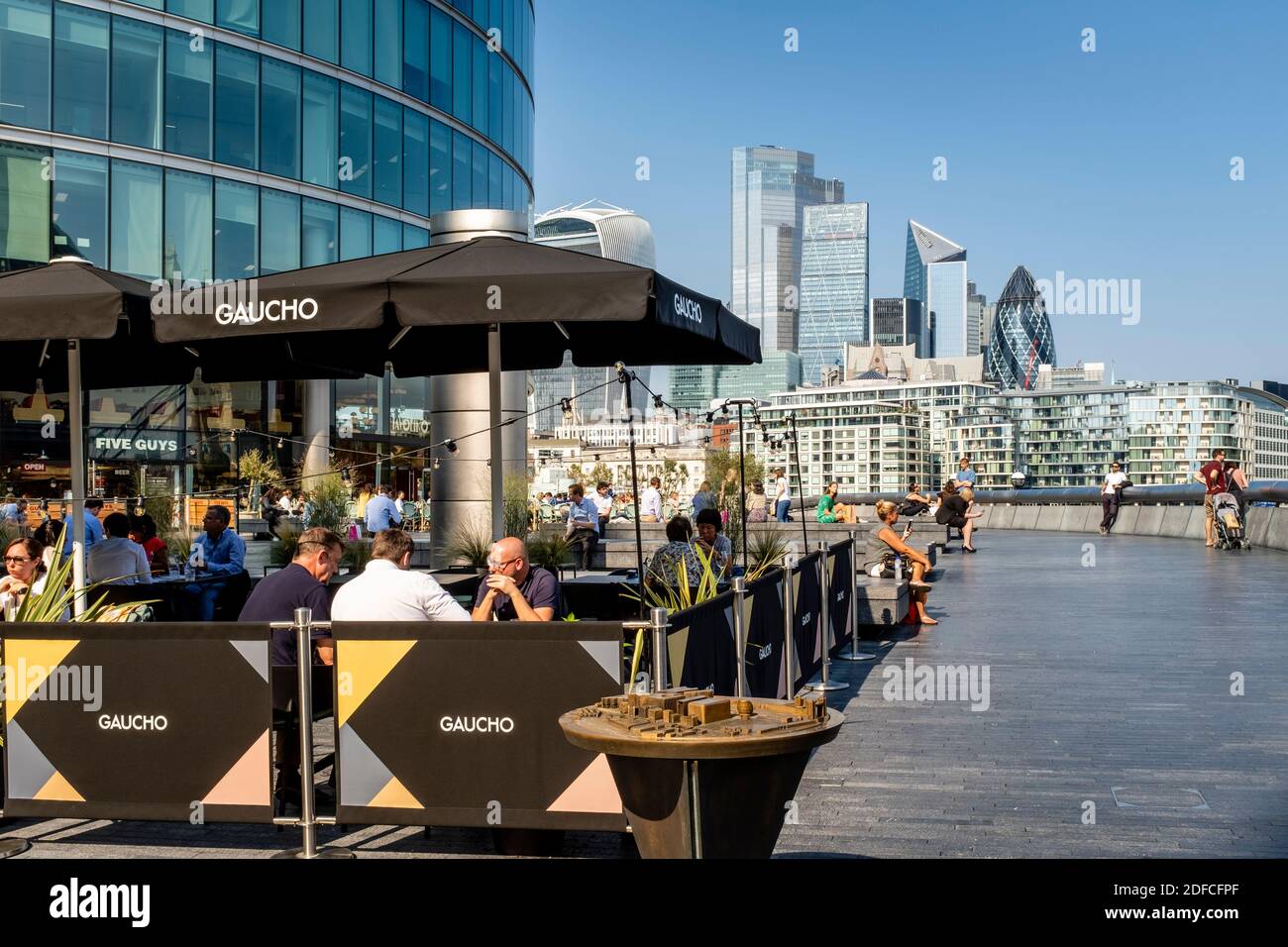 People Eating Outdoors At The Gaucho Restaurant (Tower Bridge) With The City Of London In The Backround, London Bridge City Area, London, UK. Stock Photo