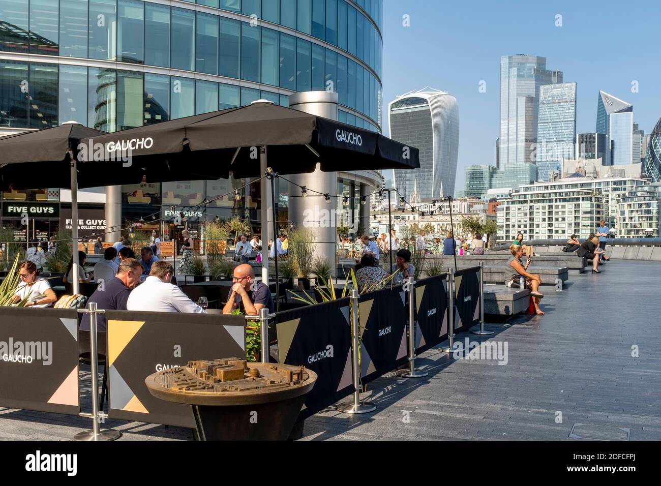 People Eating Outdoors At The Gaucho Restaurant (Tower Bridge) With The City Of London In The Backround, London Bridge City Area, London, UK. Stock Photo