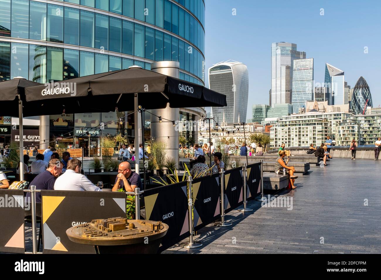People Eating Outdoors At The Gaucho Restaurant (Tower Bridge) With The City Of London In The Backround, London Bridge City Area, London, UK. Stock Photo