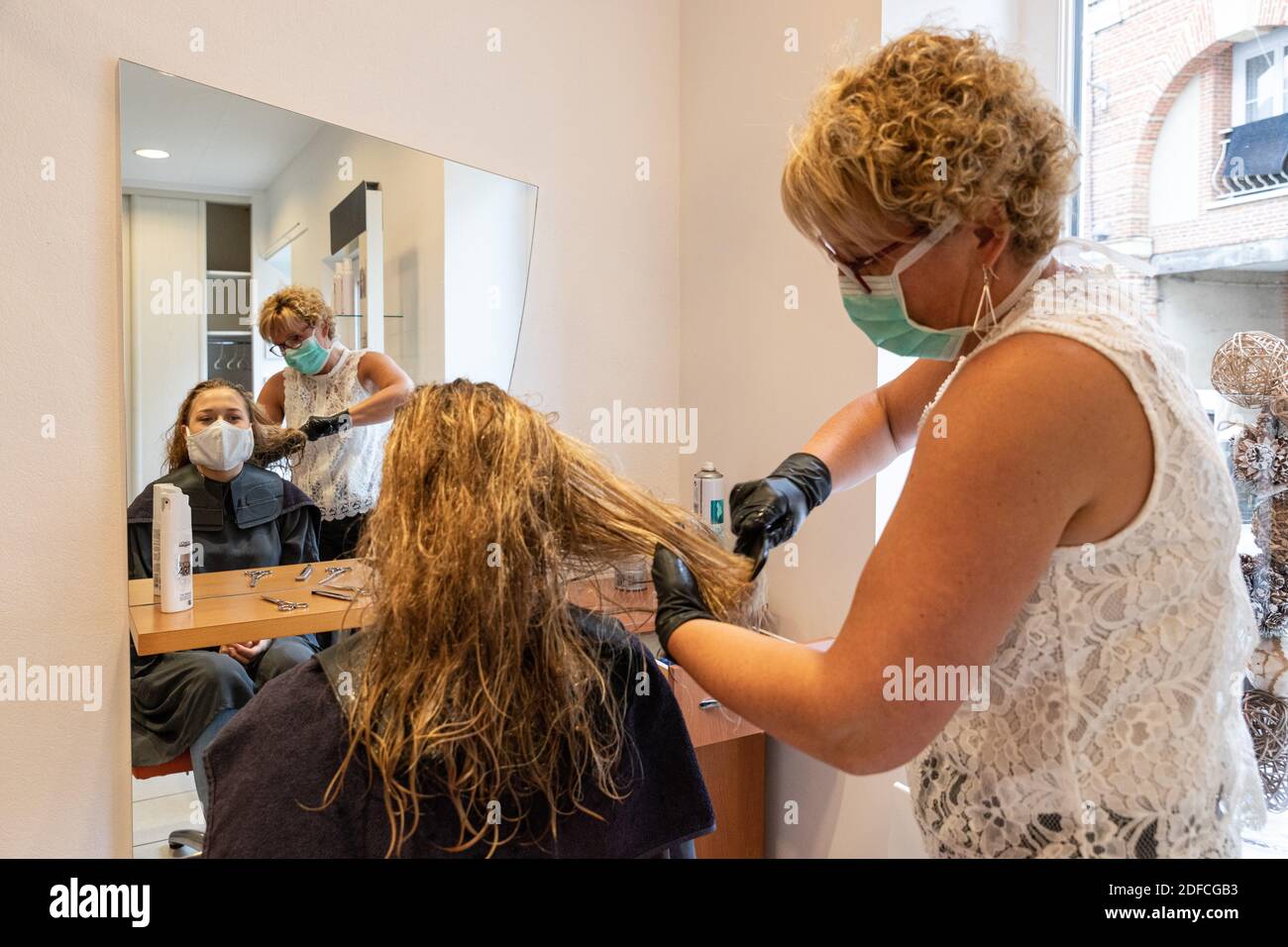 HAIRDRESSER WITH HER MASK AND GLOVES DOING A CUSTOMER'S HAIR IN AN