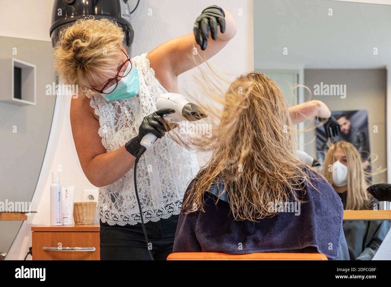 DRYING THE HAIR, HAIRDRESSER WITH HER MASK AND GLOVES DOING A CUSTOMER