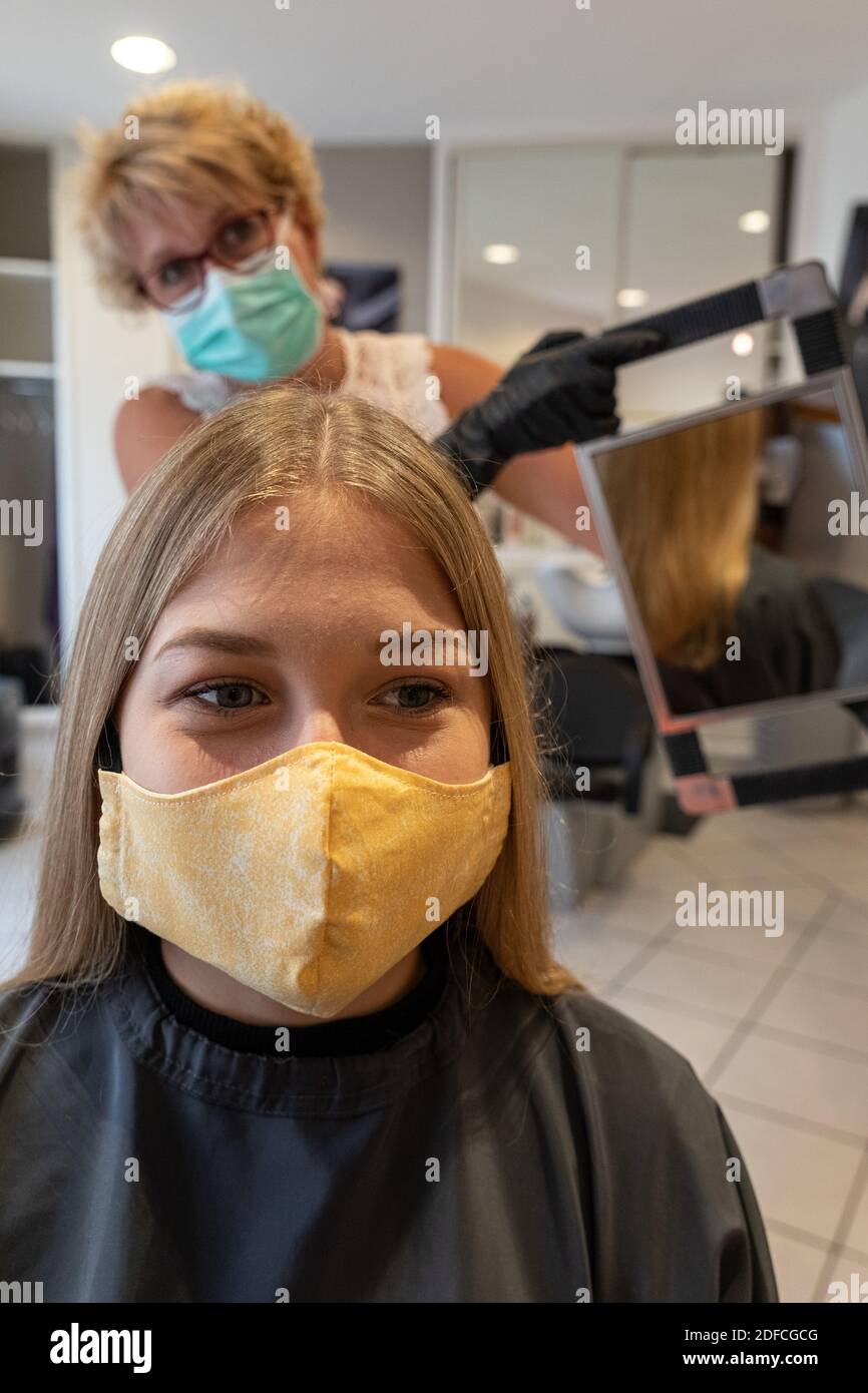 HAIRDRESSER WITH HER MASK AND GLOVES DOING A CUSTOMER'S HAIR IN AN