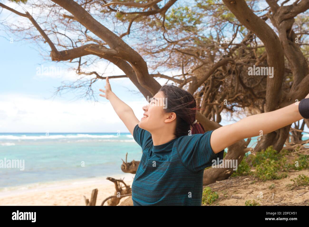 Smiling biracial teen girl with arms outstretched on beach by ocean , enjoying the breeze on tropical island Stock Photo