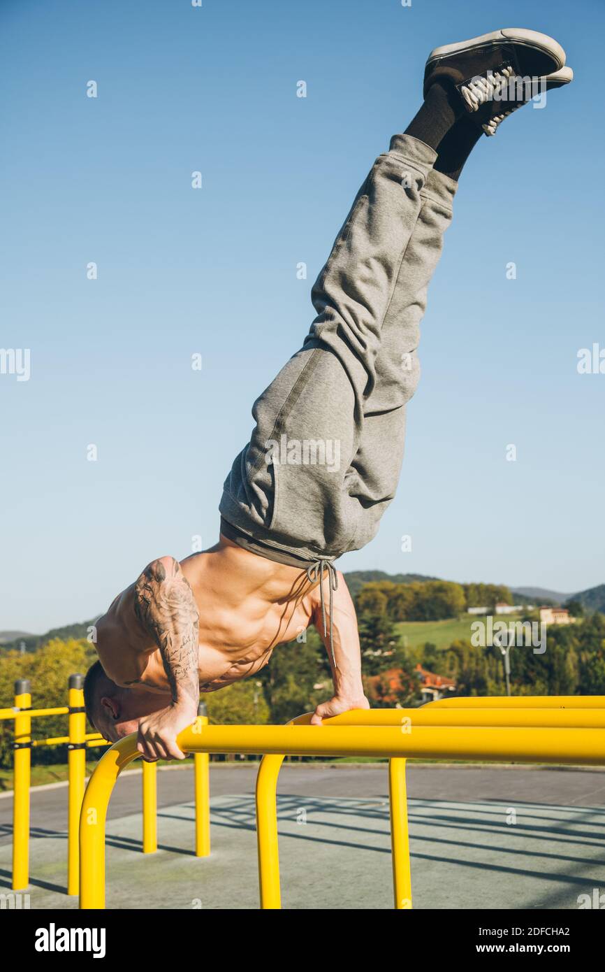 Young urban athlete doing a diagonal handstand on parallel bars at a