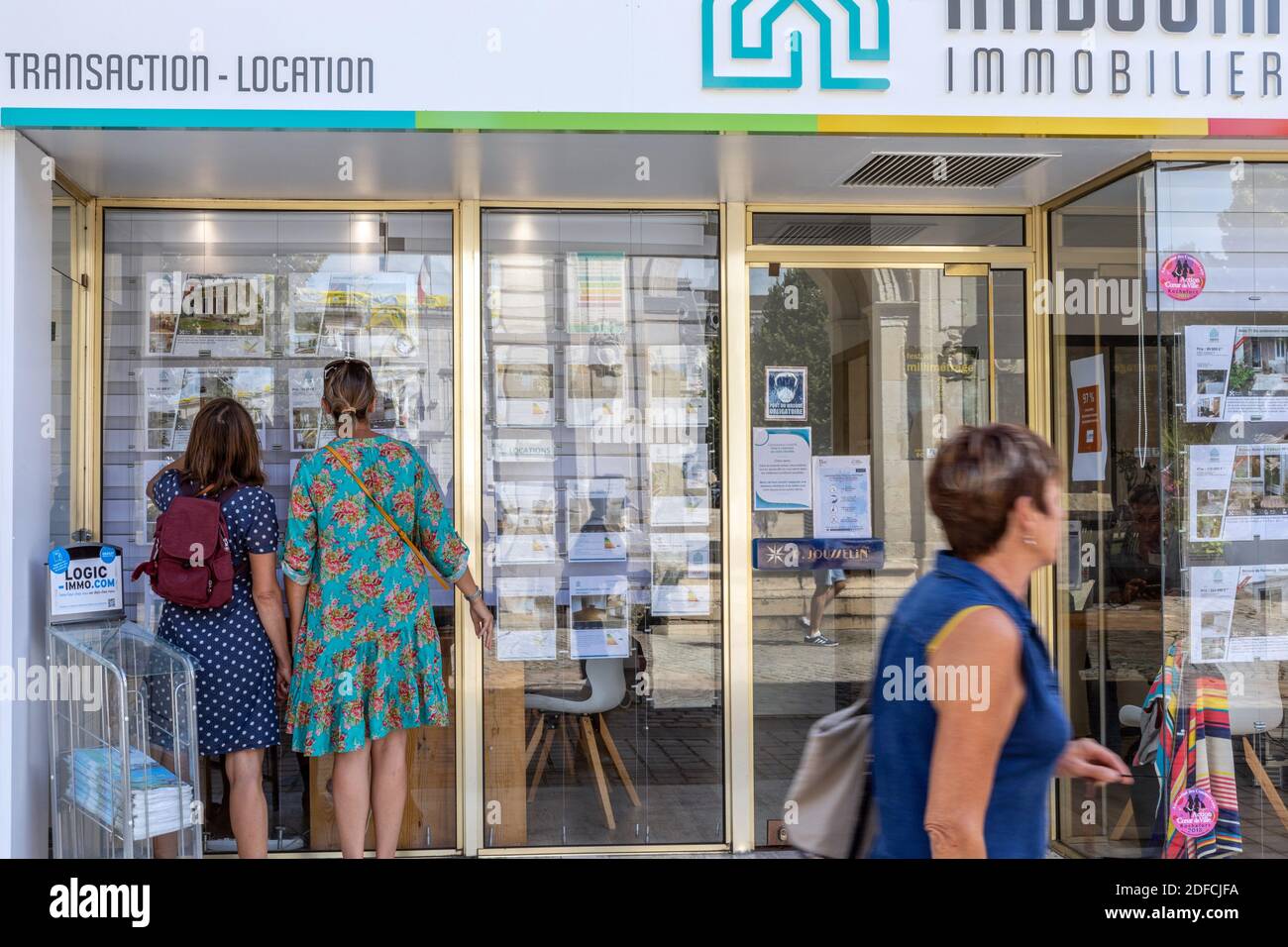 PASSERSBY IN FRONT OF THE STOREFRONT WITH REAL ESTATE ADS, REAL ESTATE