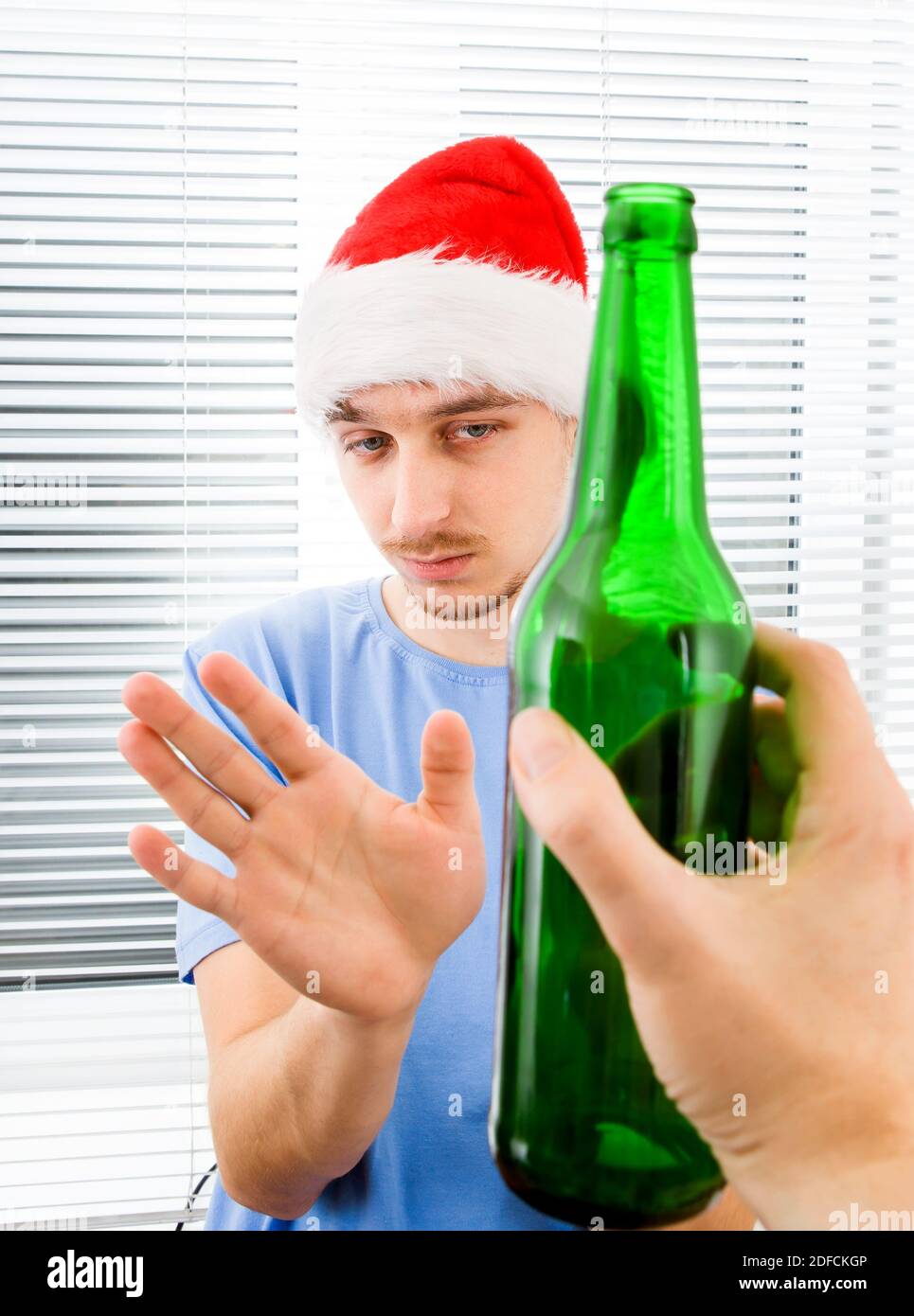 Young Man in Santa Hat refuse a Bottle of the Beer on the Jalousie Background Stock Photo