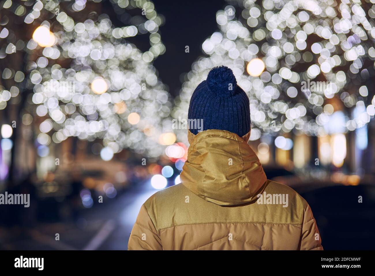Christmas holiday in city. Rear view of young man against illuminated street with shops. Prague, Czech Republic. Stock Photo