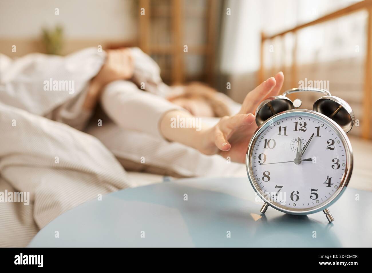 Close-up of alarm clock ringing on the table with woman sleeping in bed in  the background Stock Photo - Alamy