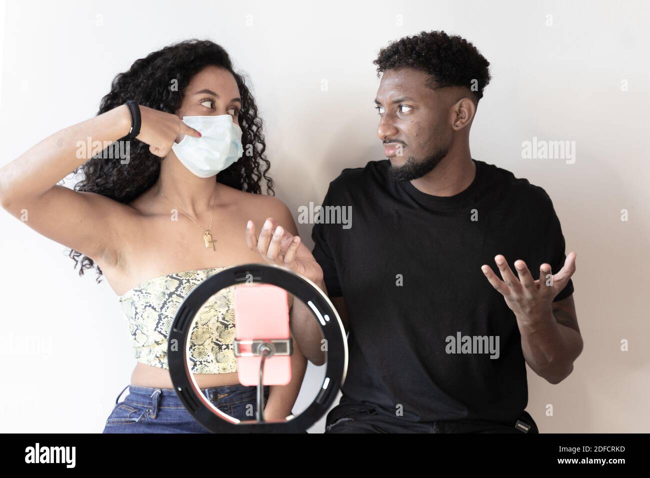 Girlfriend ordering her boyfriend to put is mask on. Friends have different opinions in wearing or not the mask. Influencers are recording a video. Te Stock Photo