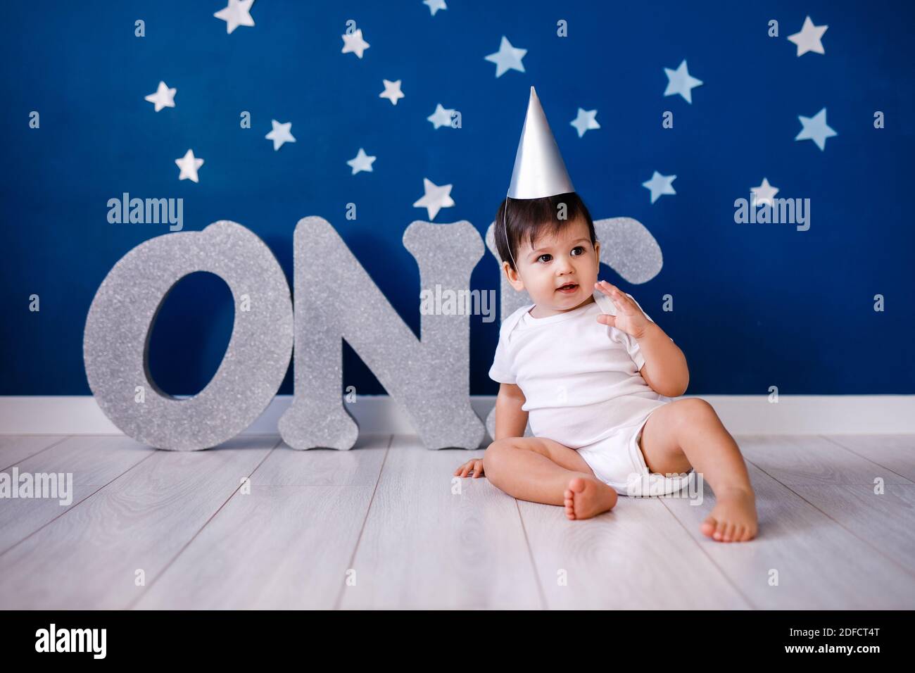 Baby boy of one year old wearing a white body and a festive paper hat sits