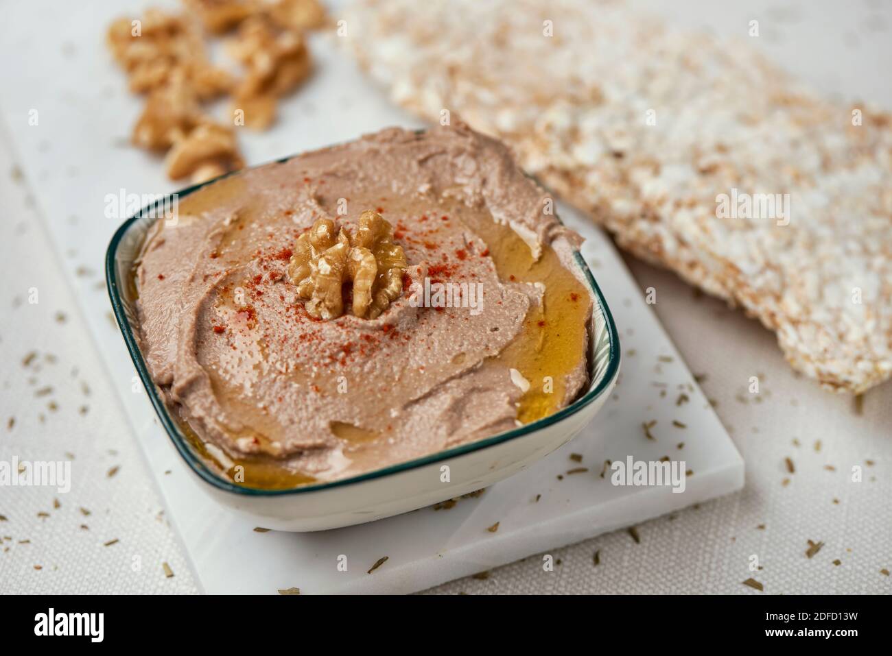 closeup of a bowl with an appetizing hummus, made with chickpea, walnut and rosemary, on a table, next to some puffed rice cakes Stock Photo