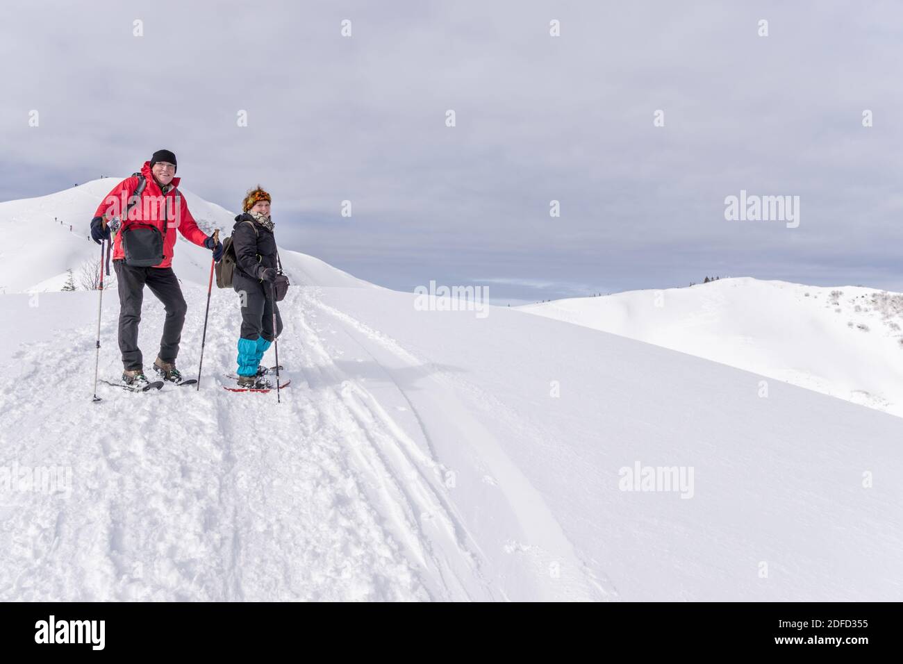 Senior couple is snowshoe hiking in alpine snow winter mountains. Allgau, Bavaria, Germany. Stock Photo