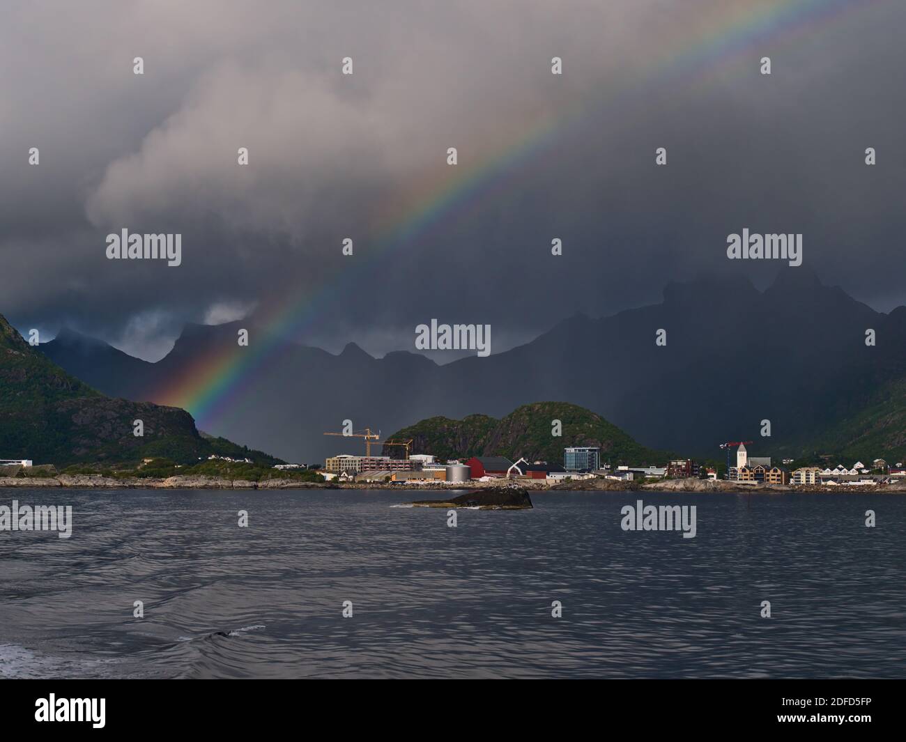 Stunning strong and colorful rainbow above fishing village Svolvær on the coast of Austvågøya island, Lofoten, Norway with rugged mountains and clouds. Stock Photo