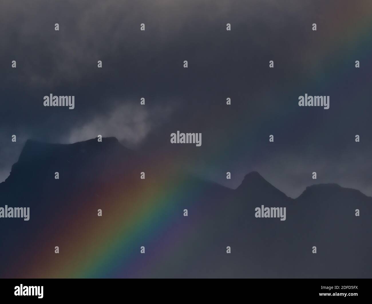 Closeup view of strong and colorful rainbow with rugged mountains in background on stormy day in late summer near Svolvær, Austvågøya, Lofoten, Norway. Stock Photo