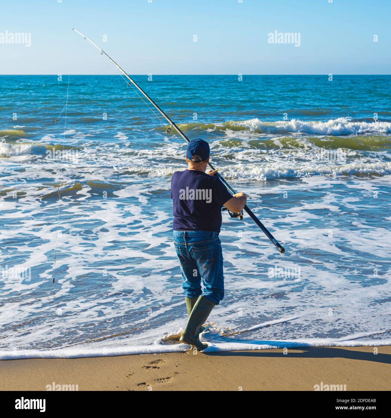 Fisherman is standing in shallow and fishing. He is throwing forward spoon Stock Photo