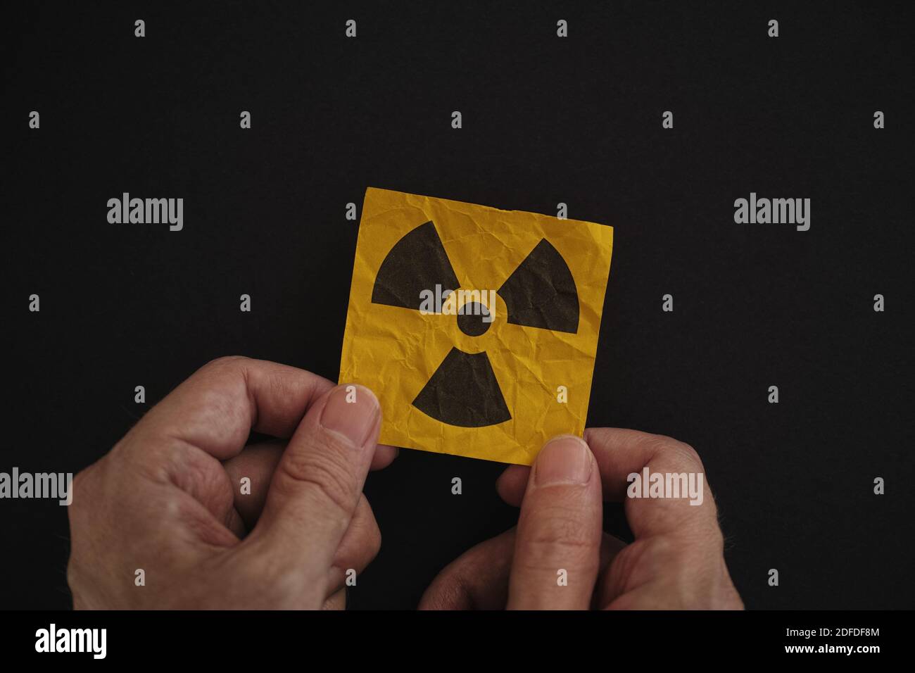 Man holding a radiation warning sign in his hands against a black background. Low key. Stock Photo