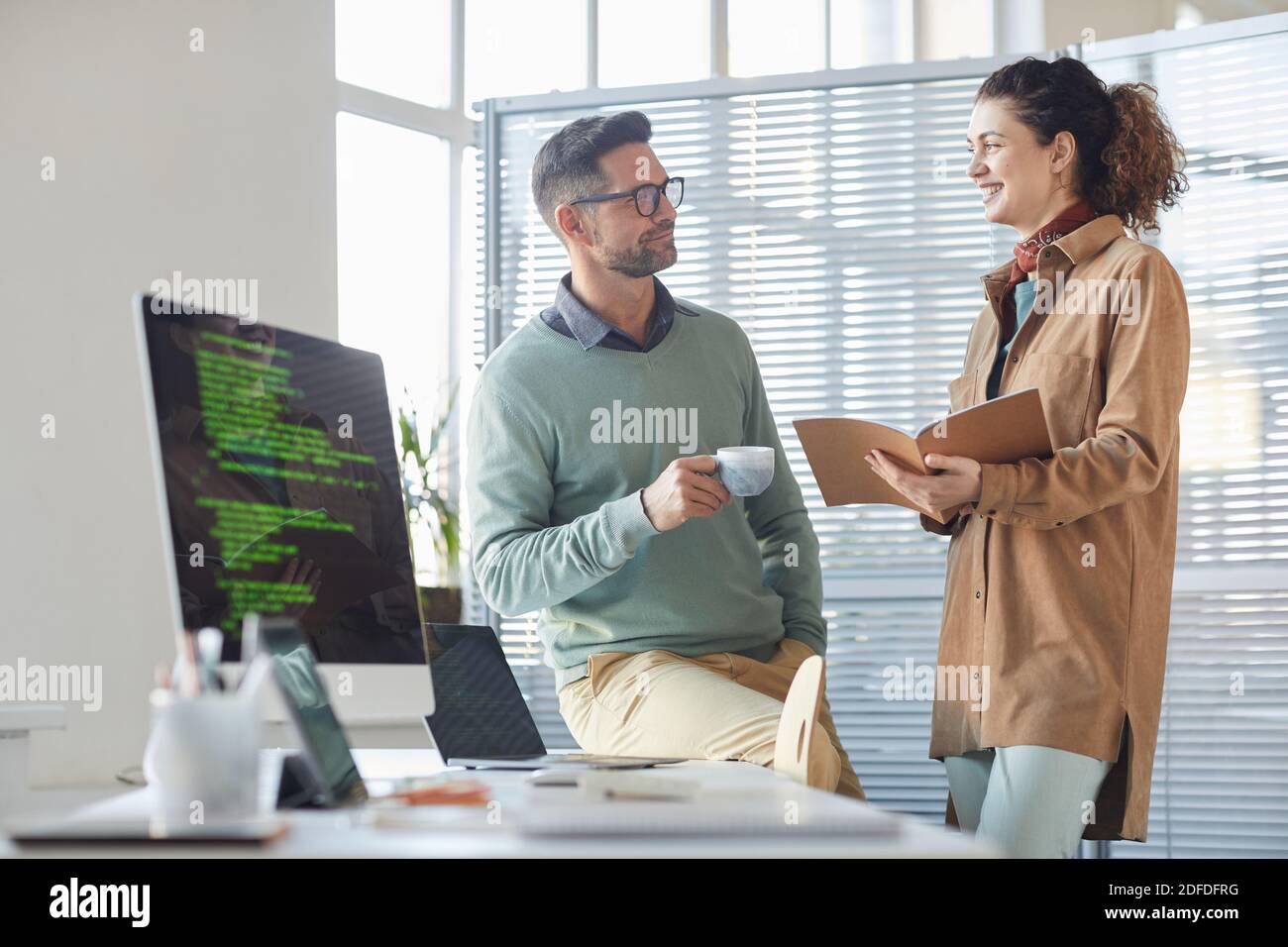 Mobile apps developers discussing work together standing near the table with computer at office Stock Photo
