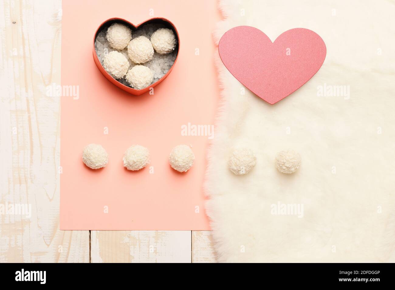 Heart shaped box with coconut balls and paper heart, top view. Valentines  day concept. Sweet surprise, gift, present, symbol of love. Coconut balls  on light wooden, pink and white furry background Stock