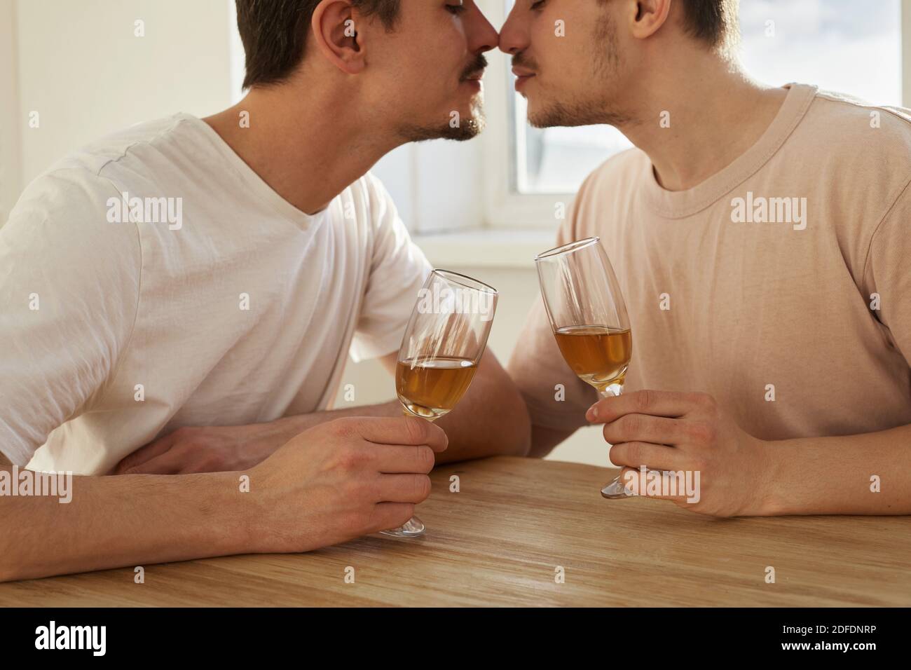 Gay couple of men drink wine from glasses and kiss at home Stock Photo