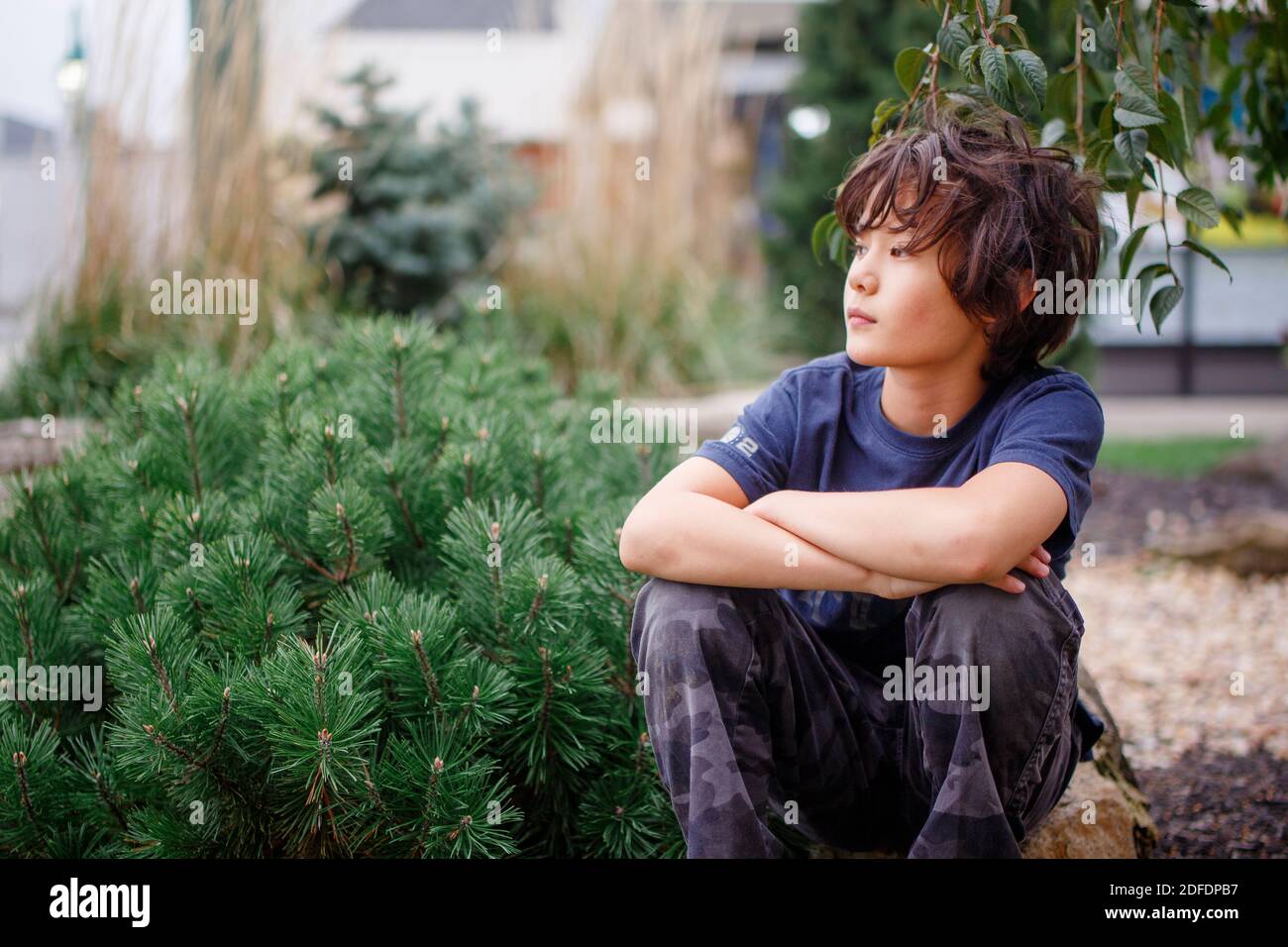 portrait of a beautiful boy sitting outside with a faraway look Stock Photo