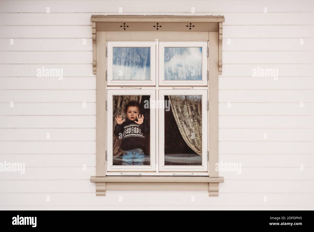 Little boy standing on window frame stuck at home in quarantine covid Stock Photo