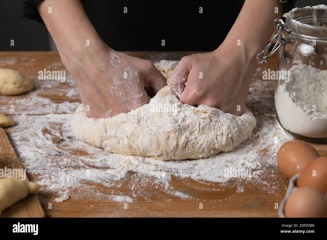 Young beautiful woman kneading dough at a wooden table in kitchen. Housewife hobbies concept. Stock Photo