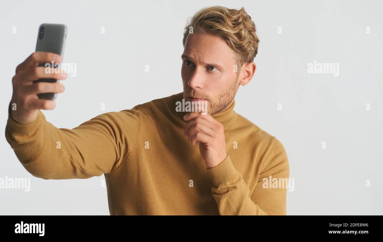 Handsome stylish bearded man taking selfie on smartphone over white background. Male model posing in studio Stock Photo