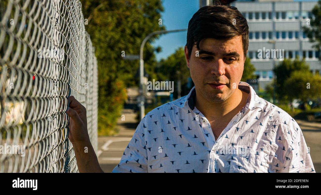 Portrait of real life man looking down holding fence. Stock Photo