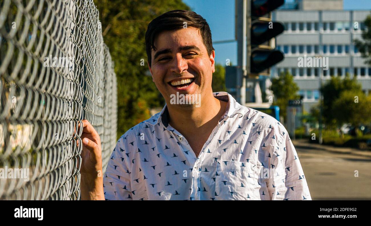 Real life man smiling for camera holding fence outdoors. Medium shot. Toothy smile. Stock Photo