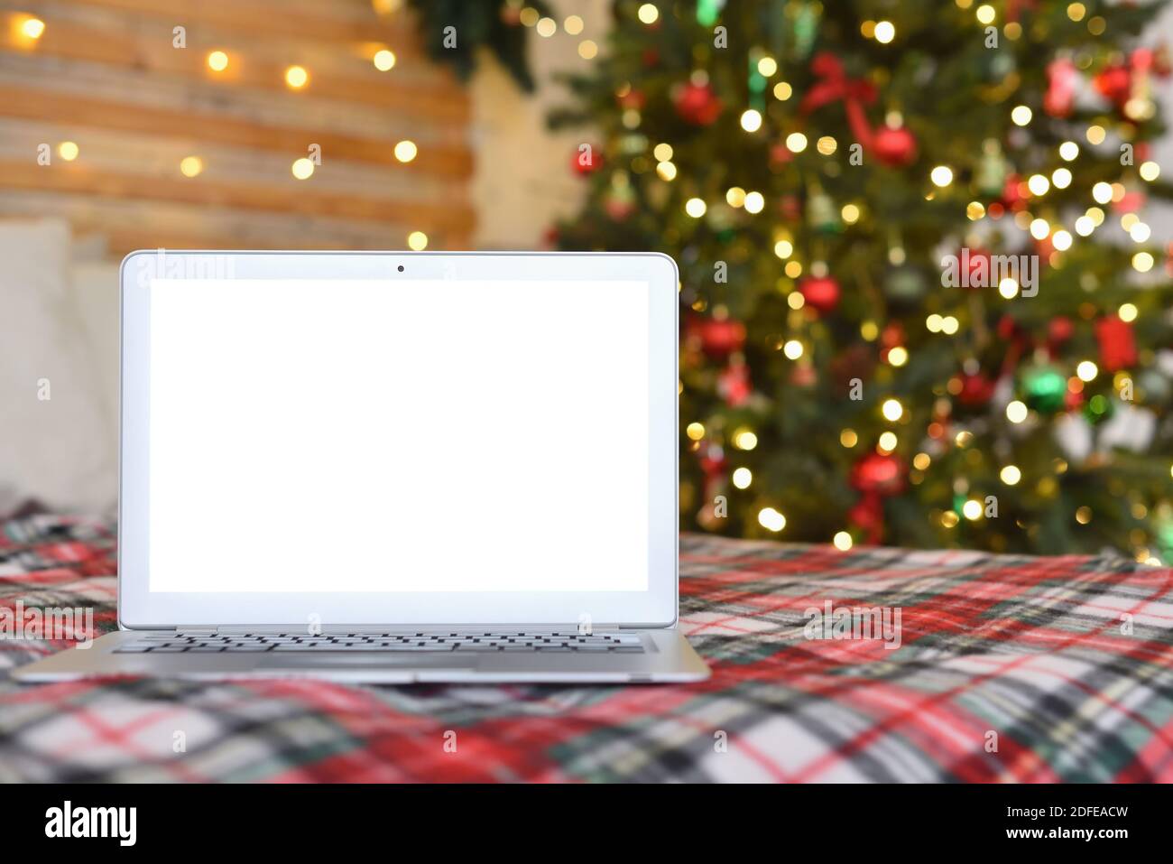 Laptop with blank screen on bed with plaid and Christmas lights Stock Photo
