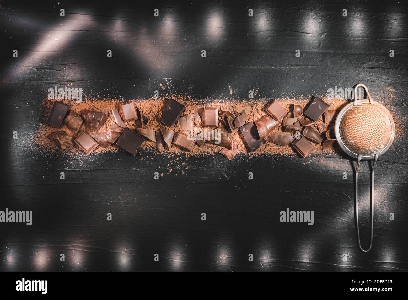 Pieces of different types of chocolate, mix of dark and milk chocolate scattered over sprinkled cocoa powder top view. Stock Photo