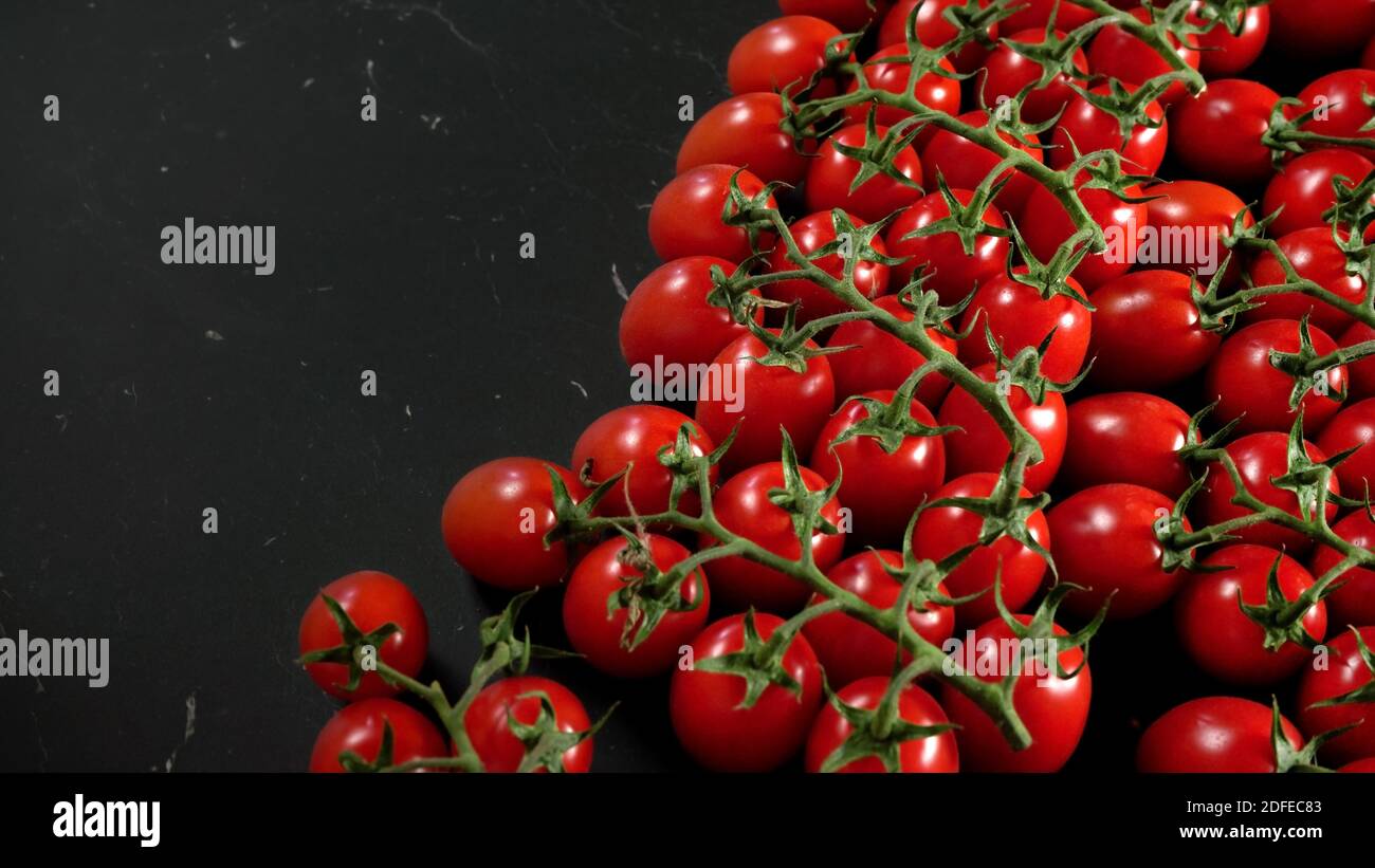 Bright red cherry tomatoes with green leaves on black marble like board ...