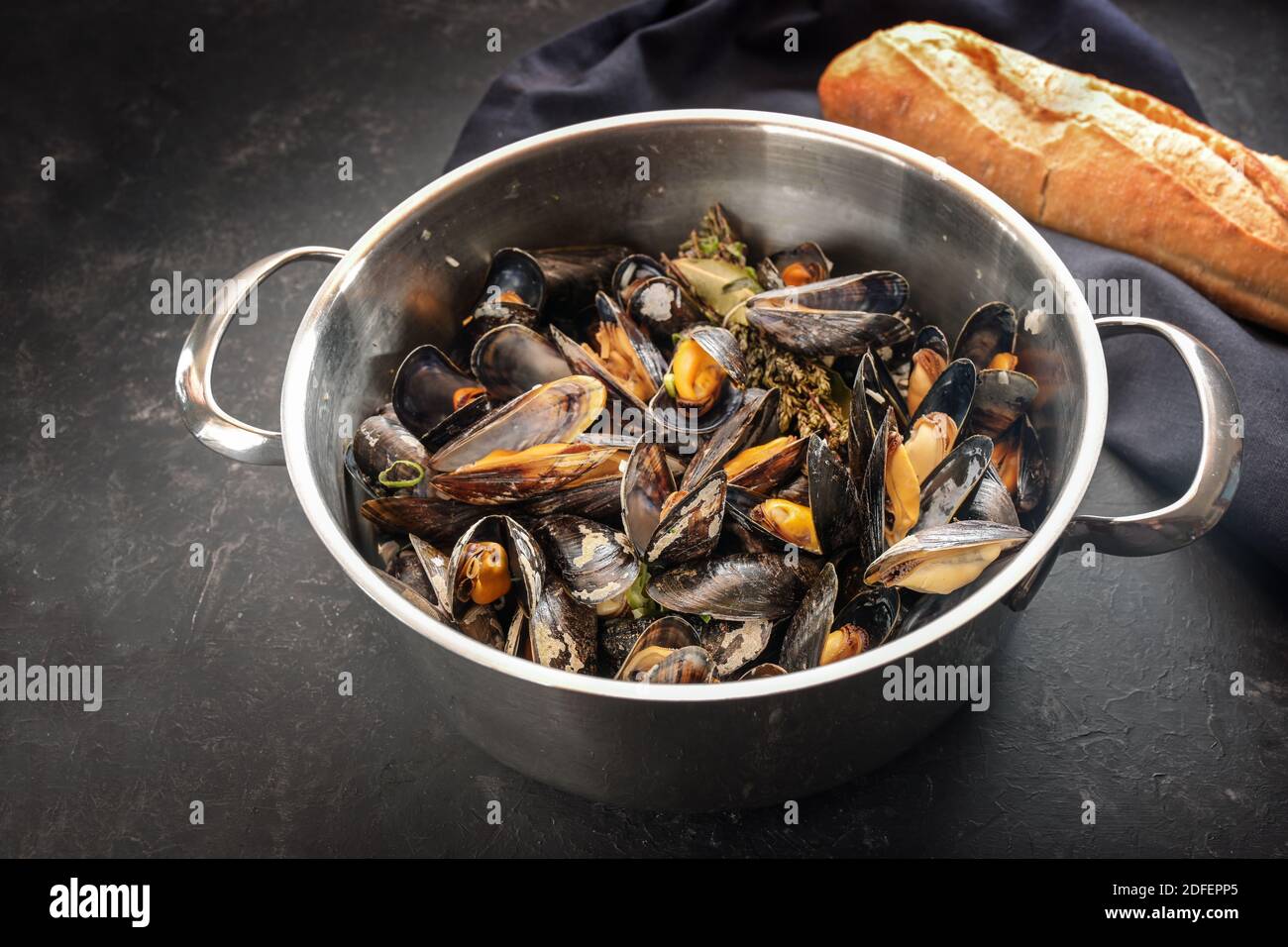 Freshly cooked mussels served in a steel pot with bread, on a dark slate table, delicious seasonal seafood meal, copy space, selected focus, narrow de Stock Photo