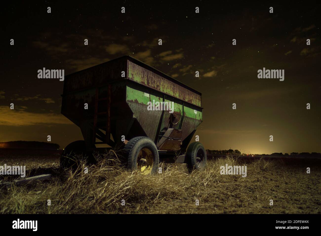 An old gravity wagon used in a small grain operation rests under the stars in a field.  Taken near Cortland, Indiana.  Lighting provided by lume cube. Stock Photo