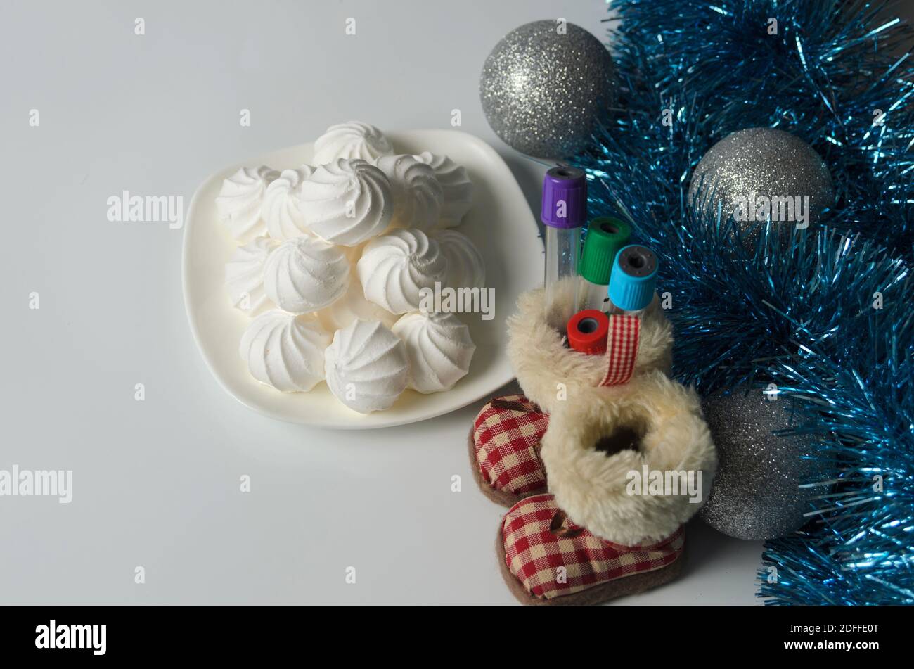 A few meringues on a plate with Christmas decorations and medical test tubes on a white table. Selective focus. Stock Photo