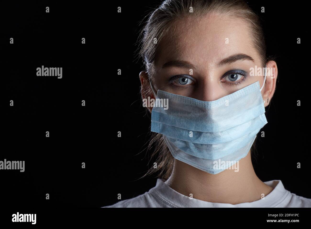 young sad woman in medical mask on black background looking at camera ...