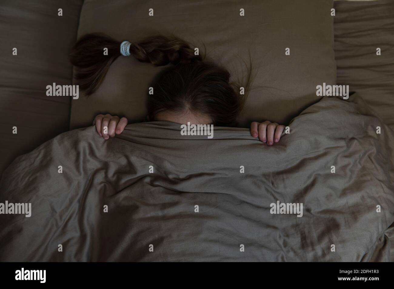 Girl with dark hair hides in bed with fear. high quality Stock Photo