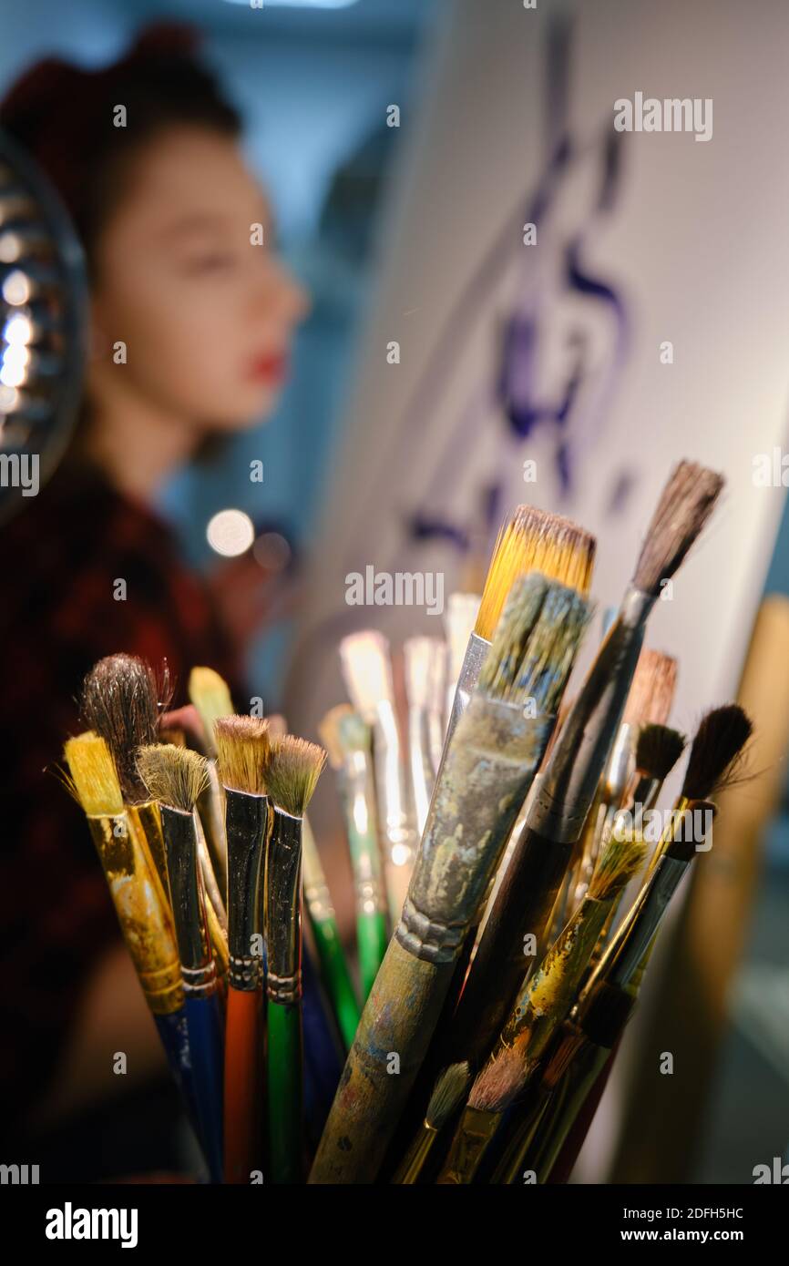 young pretty woman artist with brush near easel draws picture, defocused image Stock Photo