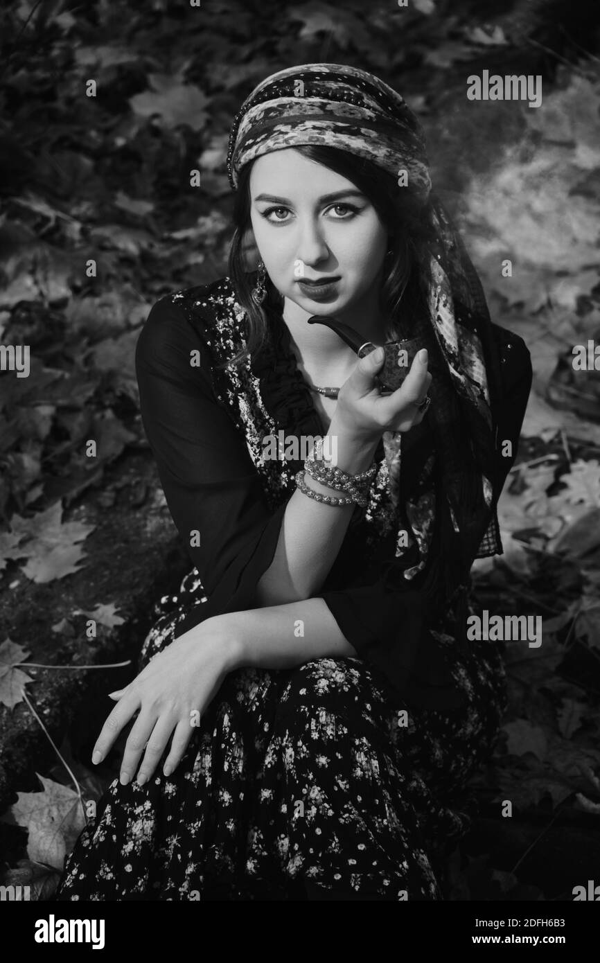 young gypsy woman smoking pipe in autumn forest, looking at camera